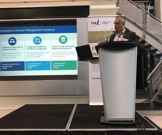 Presenting at the TSX Tech Investor Day. Standing behind a podium and delivering a PowerPoint.